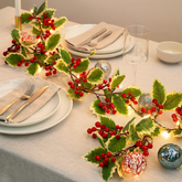 Christmas Holly Berry Garland with LED Lights – Festive Table Decoration on a dining table with dishes and lights.